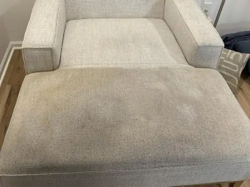 A pale fabric chaise with a soiled seat below a cleaner back cushion