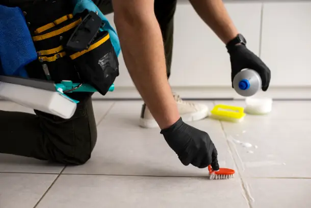 A gloved hand scrubbing a grout line on a tile floor